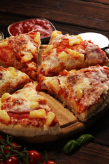 Delicious pizza with pineapple, ham slice, bacon slice, mozzarella cheese, pizza sauce on rustic background for fast food and ready to eat concept