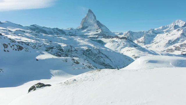 Blue Matterhorn Mountain and Standing Hiker in Winter Day. Swiss Alps, Switzerland. Low Level Flight Over Man. Aerial View. Drone Flies Forward