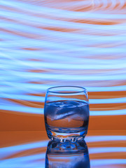 Misted up glass of cold water with blue ice on an orange background