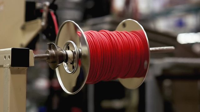 A machine rolling a red plastic wire on a metallic bobbin coil at a stock-wire factory. Close-up shot.