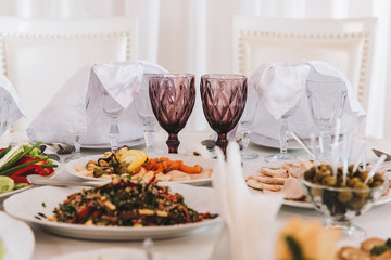Two beautiful glasses for bride and groom at a wedding, on a set up table full of food