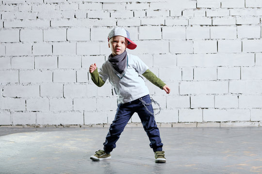little child boy model posing in fashionable rapper clothes. studio, brick wall background. Cool young kid dancing break dance.Hip-hop style.