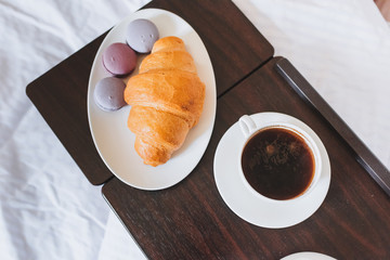 oung beautiful woman is enjoying her breakfast of black coffee, croissant and French macarons served on a tray in bed
