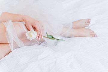 Fototapeta na wymiar Bride in a long veil lying in bed holding a tulip flower