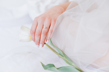 Bride in a long veil lying in bed holding a tulip flower