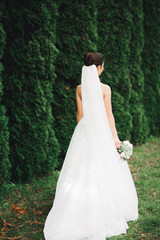 Obraz na płótnie Canvas Beautiful bride in elegant white dress holding bouquet posing in park