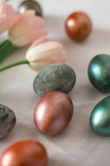Beautiful colored shiny easter eggs on the white plate. Pink tulips flowers bouquet. Happy easter concept.