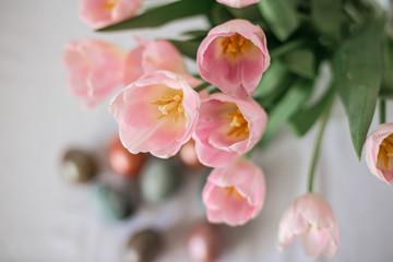 Obraz premium Beautiful colored shiny easter eggs on the white plate. Pink tulips flowers bouquet. Happy easter concept.
