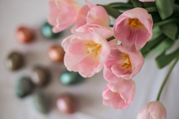 Beautiful colored shiny easter eggs on the white plate. Pink tulips flowers bouquet. Happy easter concept.