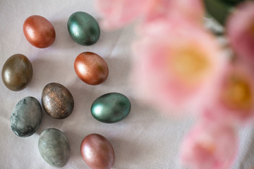 Beautiful colored shiny easter eggs on the white plate. Pink tulips flowers bouquet. Happy easter concept.