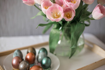 Beautiful colored shiny easter eggs on the white plate. Pink tulips flowers bouquet. Happy easter concept.