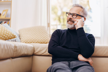 Obraz premium Senior man talking on his mobile phone at home