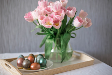 Beautiful colored shiny easter eggs on the white plate. Pink tulips flowers bouquet. Happy easter concept.