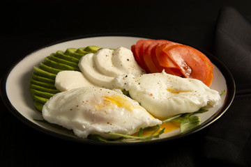 Avocado poached eggs. Healthy breakfast food and tomato on black background.