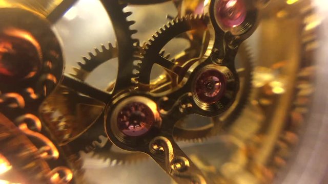 Mechanical timepiece movement. Macro close up of gears, jewels and escapement. Gold ornate design with soft edges over light background.