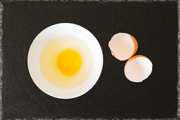 whole egg broken egg with egg shells in a bowl with black slate background