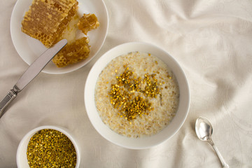 Breakfast: oatmeal with bee pollen and honey  in the white bowl on the textile background.Top view.Copy space.