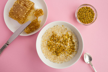 Breakfast: oatmeal with bee pollen and honey  in the white bowl on the pink background.Top view.