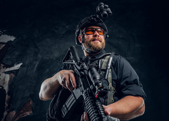 Bearded special forces soldier wearing body armor and helmet with night vision holding an assault...
