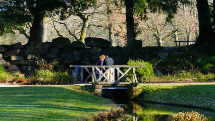 Paar steht auf einer Brücke, zärtlich und eng  beieinander, und beobachtet etwas im wasser