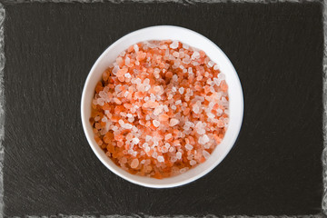 Himalayan mountain pink rock salt on a black slate plate in a round bowl