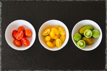 Exotic tomatoes rosa red yellow and green tomatoes in bowls on a black slate background