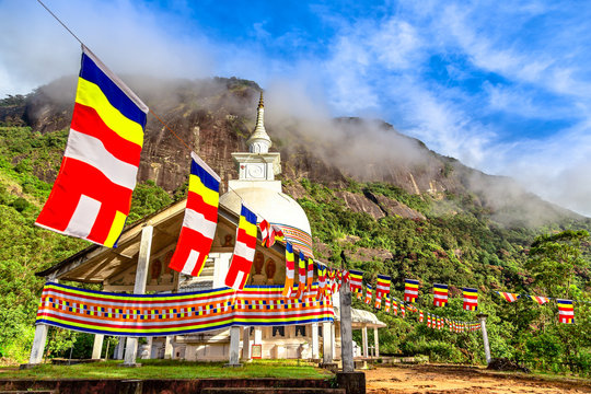 Colorful buddhist flags with stupa temple, green mountains and blue sky in the background, on the way to the top of Adam's peak, Sri Lanka