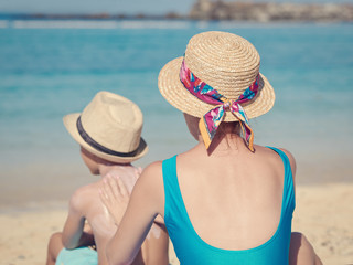 Mom is covering her son with sunscreen on the beach during the summer holidays, preventing sun burns.