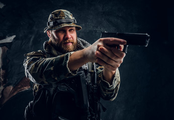 Brutal special forces soldier in the military camouflaged uniform holding a gun and aiming at the...