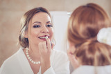 Young European woman with beautiful hairstyle and makeup is standing in front of the mirror and gathering for a date.
