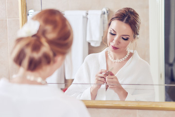 Young lady is using nail file in her bathroom in front of the mirror to make a manicure.