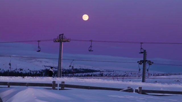 Person riding a ski lift in Idre Fjäll in Sweden during a colorful sunset. With a full moon, the same night of the blood moon.