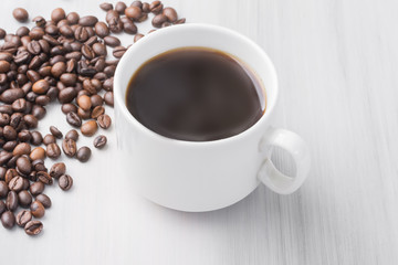 a cup of black natural coffee, coffee beans, on a light wooden table