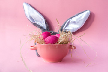 pink Easter eggs in generic plate ,gray  rabbit ears on pink background