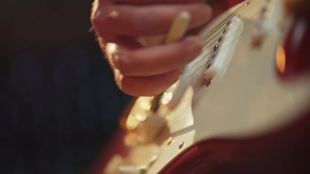 A colorful shallow depth of field extreme close up of a Fender stratocaster pick up and wammy bar with beautiful lighting as it is picked and played by a male in jeans and t-shirt.