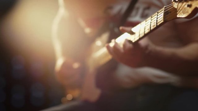 A colorful shallow depth of field close up of a Fender Telecaster finger board with beautiful lighting as it is picked over pickup and played by a male in jeans and t-shirt.