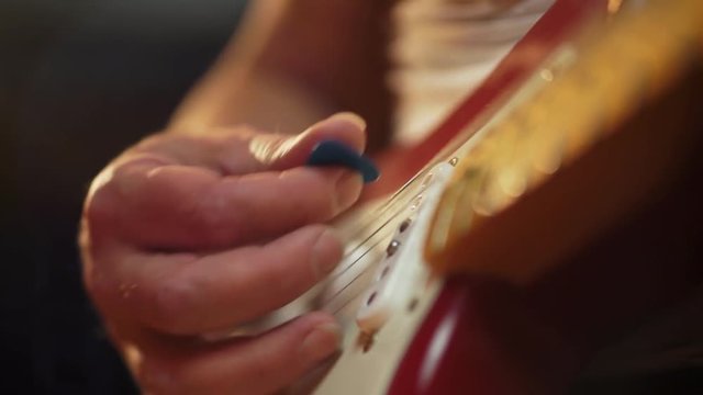 A colorful shallow depth of field close up of a Fender stratocaster pickup with beautiful lighting as it is picked and played by a male in jeans and t-shirt.