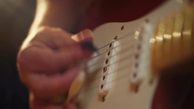 A colorful shallow depth of field close up of a Fender Telecaster with beautiful lighting as it is picked and played by a male in jeans and t-shirt.