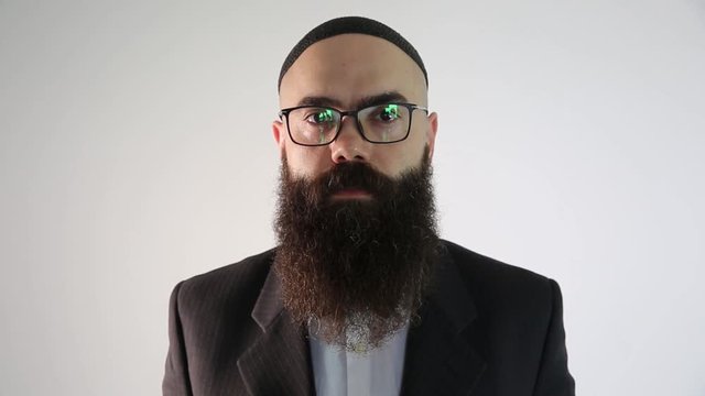 A bearded man with quip and a traditional Jewish clothing. He smiles looking at the camera.