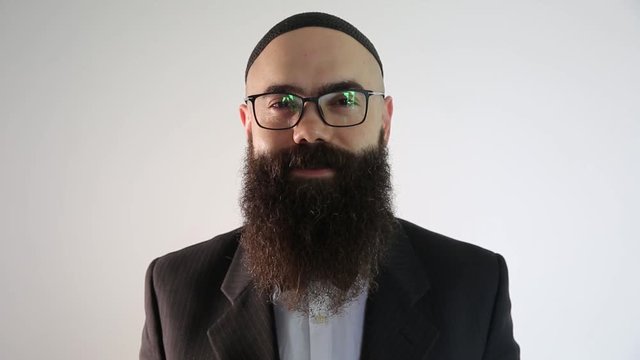 A bearded man with quip and a traditional Jewish clothing. He smiles looking at the camera.