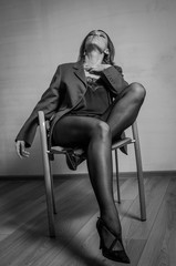 Young charming girl sitting on a chair in a jacket, pantyhose and shoes with heels