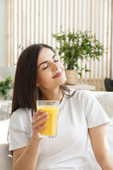 Brunette woman with closed eyes holding glass with orange juice