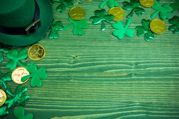 St Patricks Day frame of shamrocks, gold coins and leprechaun hat on green wood