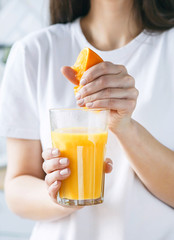 Brunette woman squeezes orange juice at the light kitchen