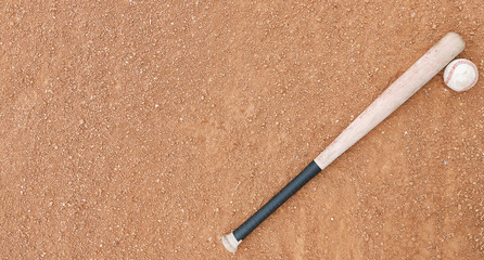 Horizontal image of old baseball bat with ball on dirt field.  Copy space beside sports equipment.