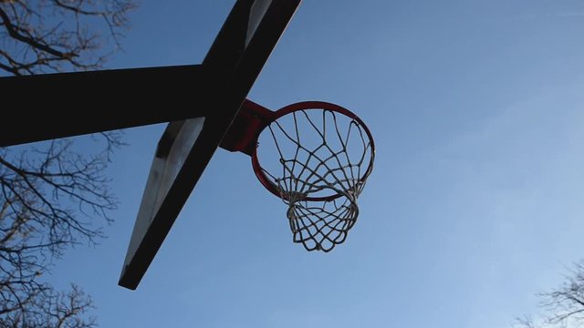 A view from below a basketball goal of lay-ups being made.  A blue sky is present in the park