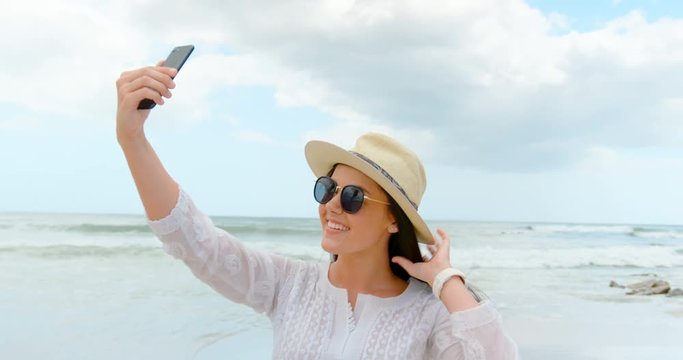 Side view of young caucasian woman taking selfie with mobile phone at beach 4k