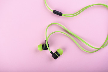 Green headphones or earphones isolated on a pink background