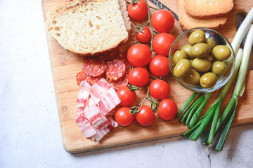 The homemade white bread on a wooden board with organic bacon, cut sausage, cherry tomato, onions and green olives.Toned picture.