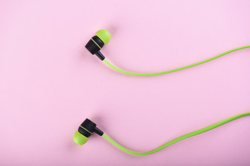 Green headphones or earphones isolated on a pink background